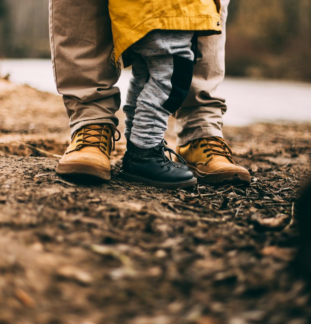 Lebensformen bejahen Füße eines Erwachsenen und eines Kindes auf einem erdigen Boden, umgeben von Natur.
