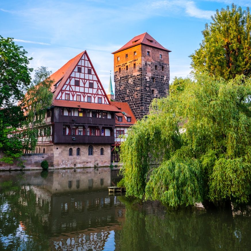 Freie Wähler Röttenbach e.V. - In der Metropolregion Nürnberg Historische Gebäude und Turm entlang eines ruhigen Gewässers mit Bäumen.
