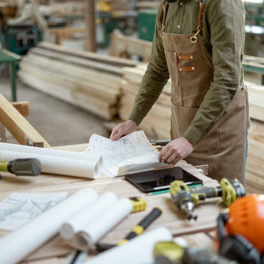 Freie Wähler Röttenbach e.V. - Für das Handwerk Ein Zimmermann arbeitet an einem Tisch mit Plänen und Werkzeugen in einer Werkstatt.